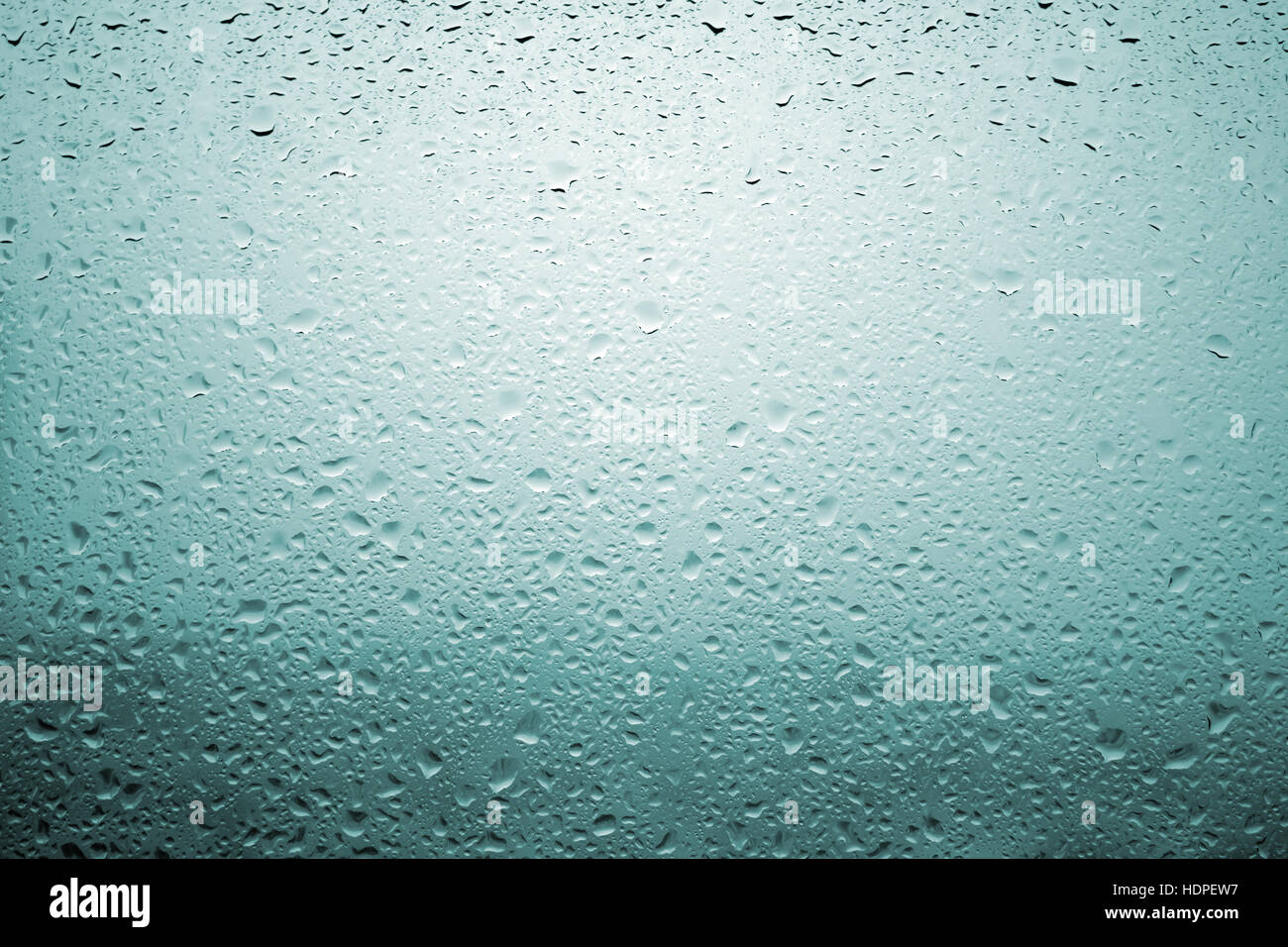 Gouttes de pluie sur une vitre de fenêtre avec paysage très diffuse de couleur bleu verdâtre Banque D'Images
