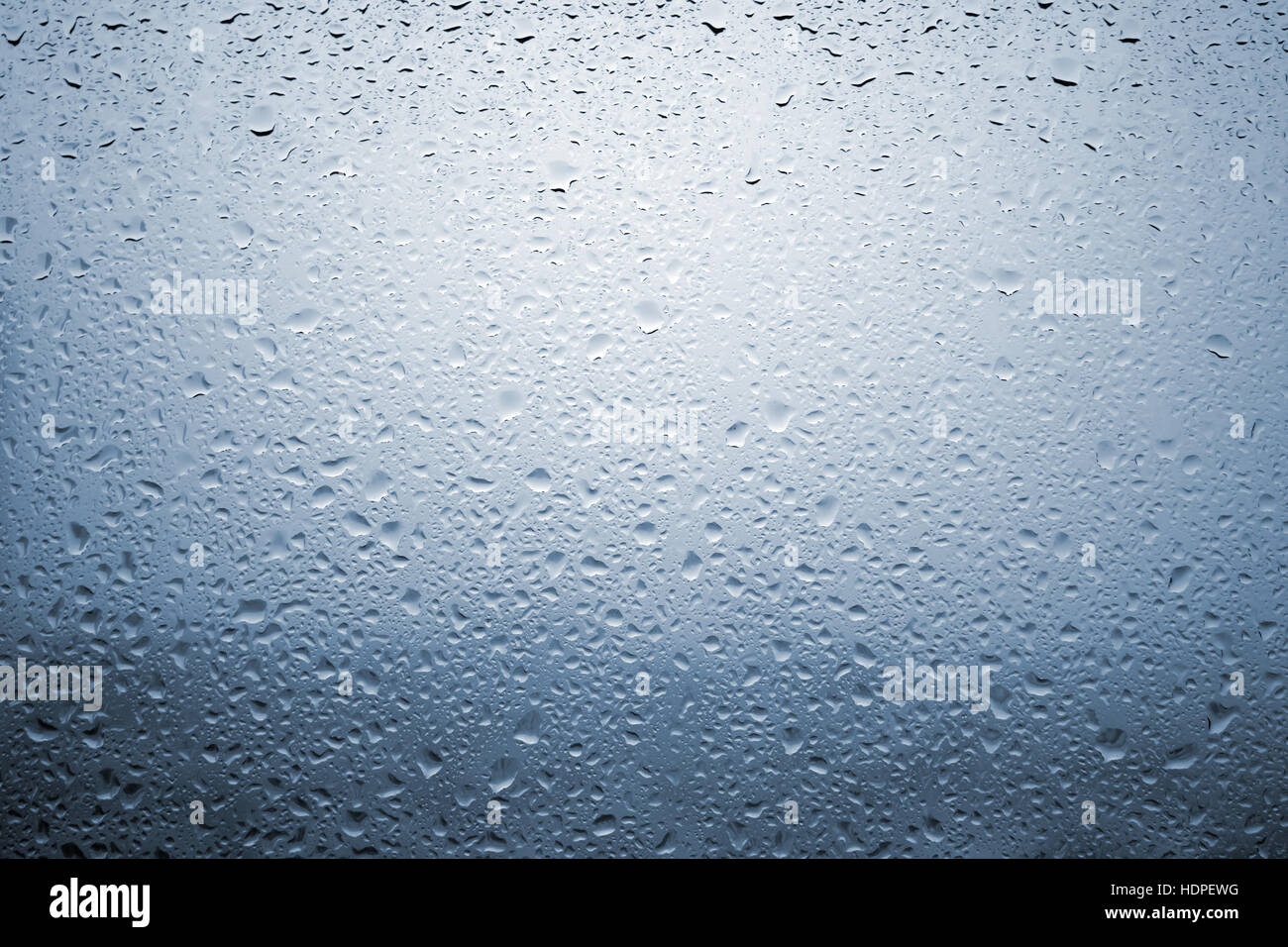 Gouttes de pluie sur une vitre de fenêtre avec paysage très diffuse de couleur bleu pâle Banque D'Images