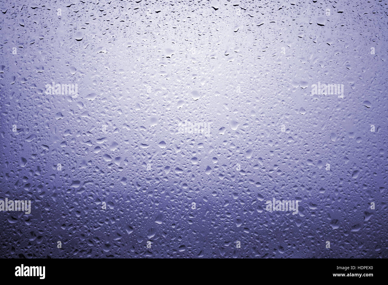 Gouttes de pluie sur une vitre de fenêtre avec paysage très diffuse de couleur bleu violacé Banque D'Images