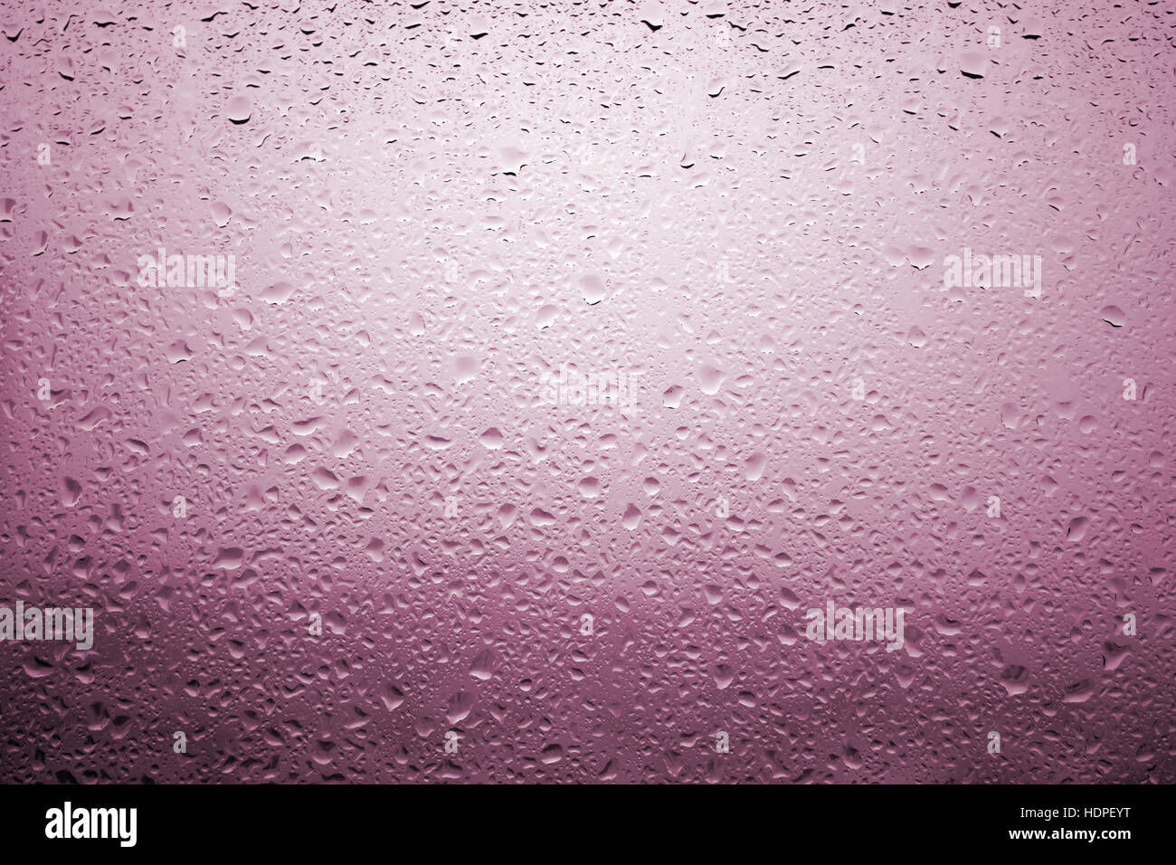 Gouttes de pluie sur une vitre de fenêtre avec paysage très diffuse de couleur rose rougeâtre Banque D'Images