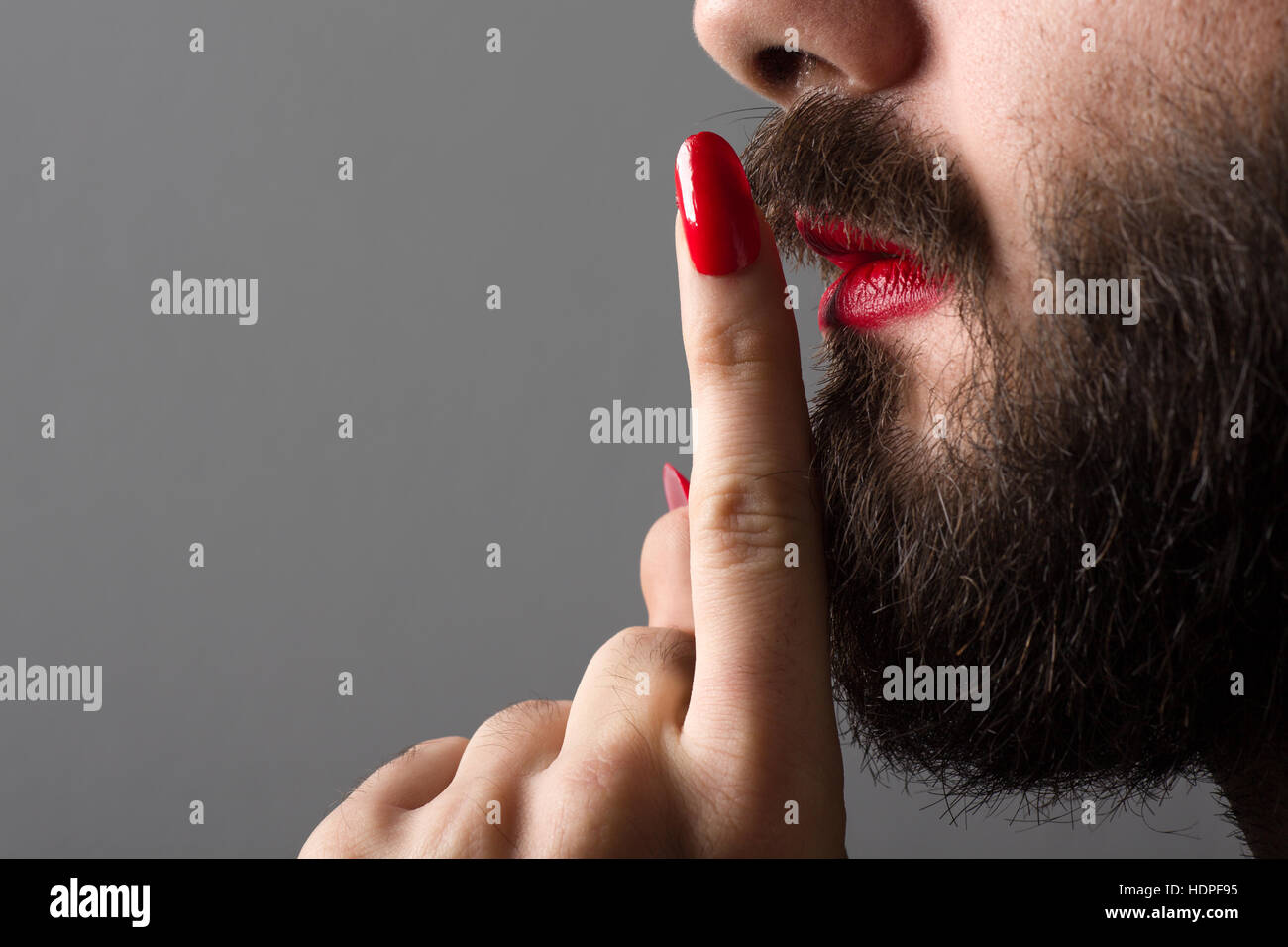 Homme barbu avec le rouge à lèvres rouge à lèvres vernis à ongles et faire de geste Silence Banque D'Images