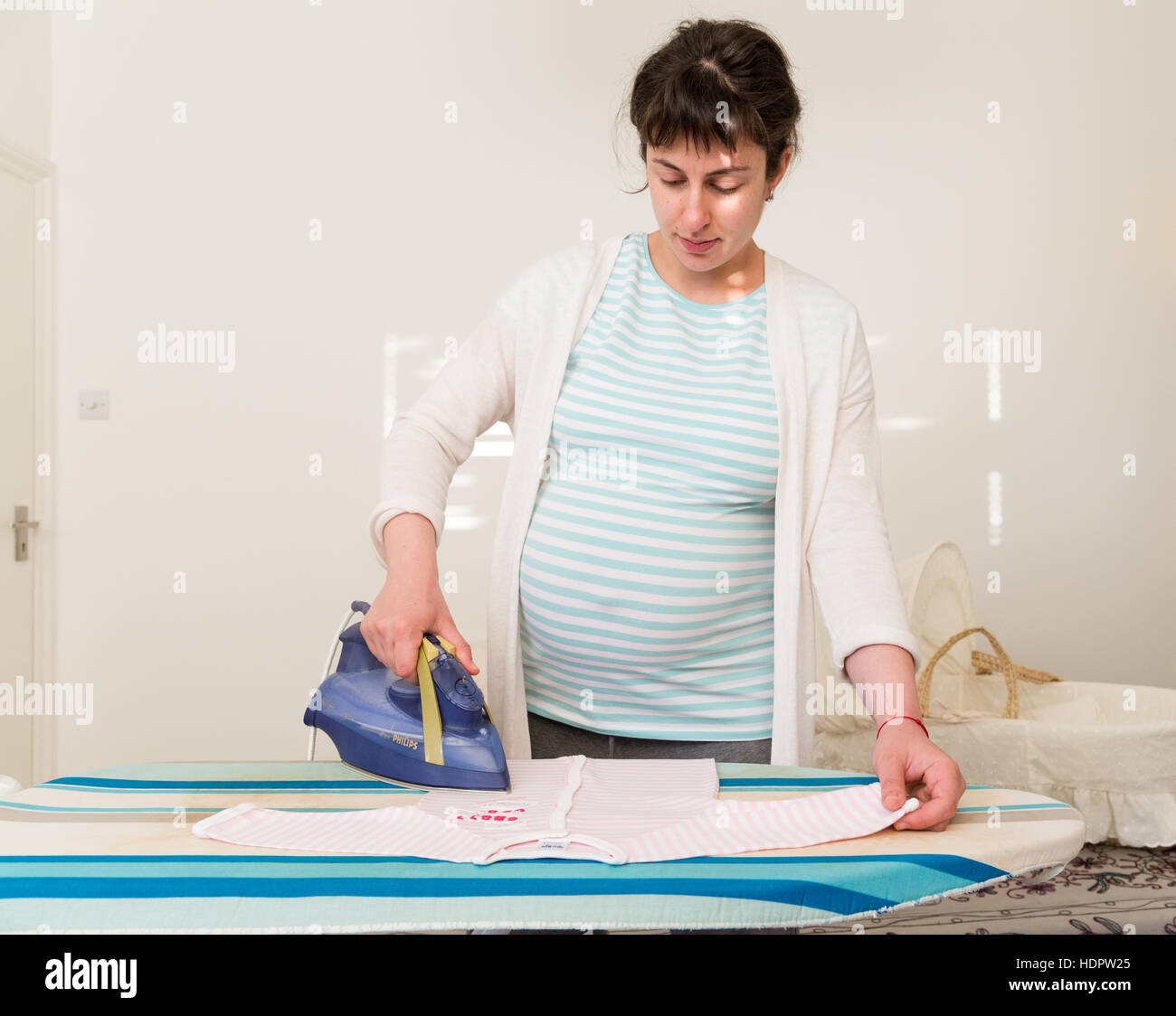 Repassage femme enceinte vêtements de bébé en prévision de l'arrivée de bébé, England, UK Banque D'Images