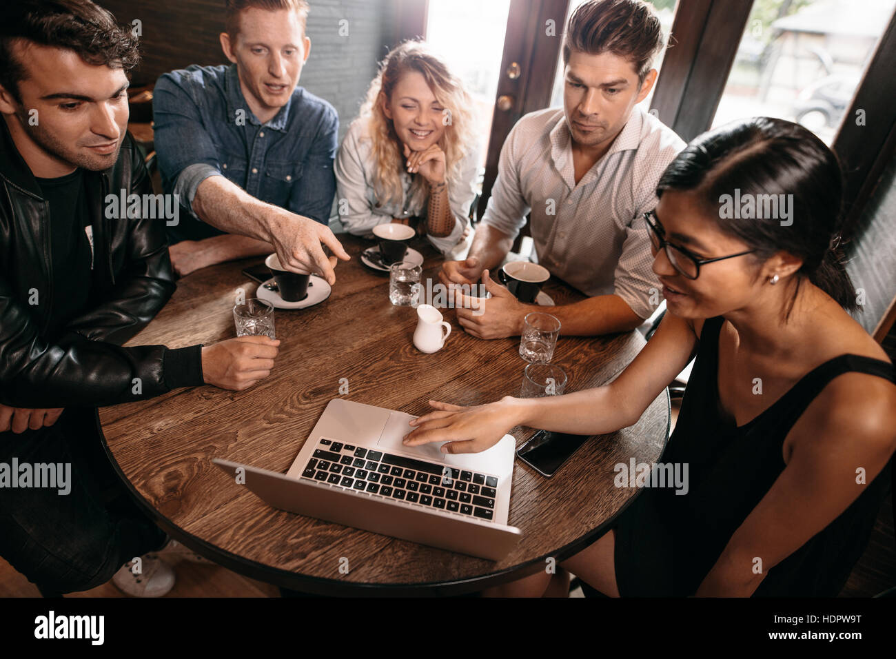 Groupe d'amis assis ensemble à café avec man pointing at laptop. Cinq jeunes gens au coffee shop Banque D'Images