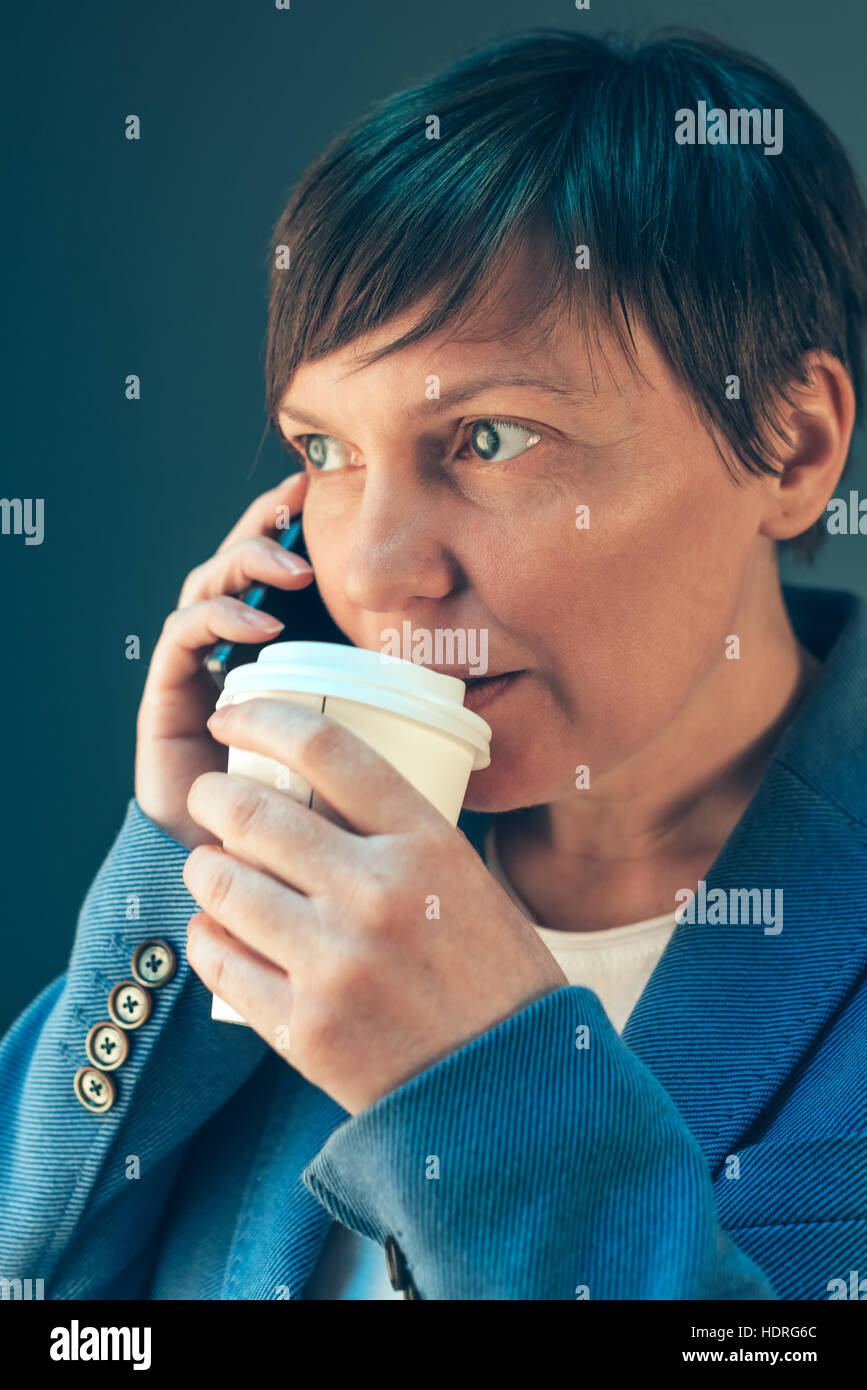 Young adult businesswoman drinking coffee pour aller et talking on mobile phone Banque D'Images