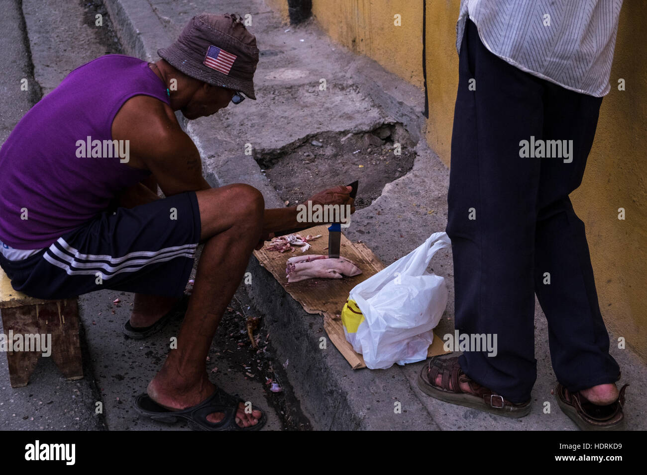 Man chopping un porcs trotter sur le trottoir à Santiago de Cuba, Cuba Banque D'Images