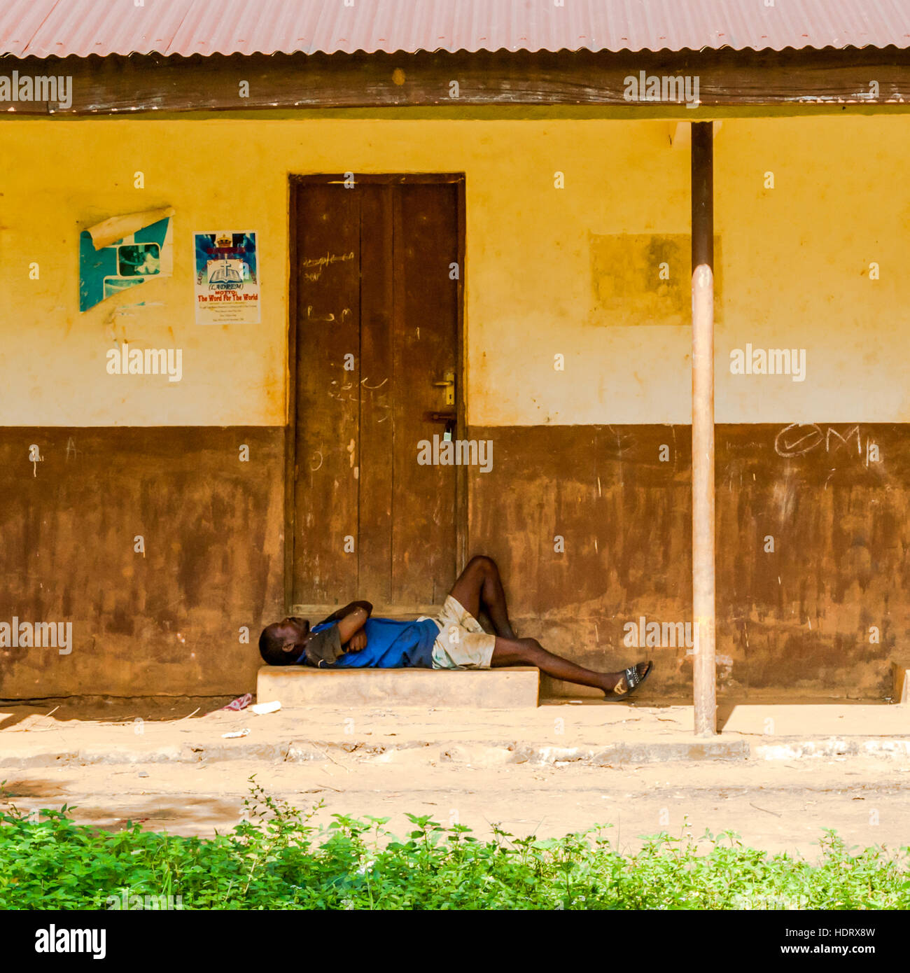 Un homme dort sur la véranda de l'école "Remembrance Harbour" sur Banana Island, Sierra Léone, entre deux portes à l'ombre du toit en tôle ondulée. Banque D'Images