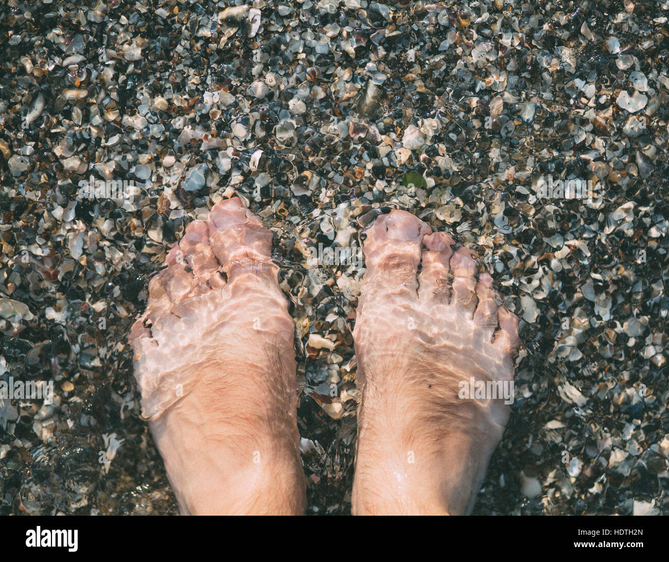 Les pieds dans l'eau claire de la mer de cailloux. Banque D'Images
