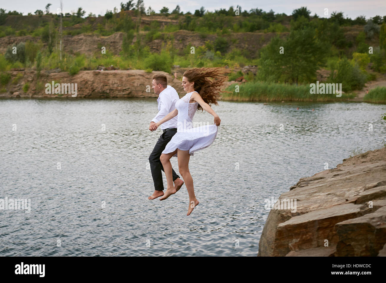 Mariée et le marié de sauter ensemble dans l'eau Banque D'Images