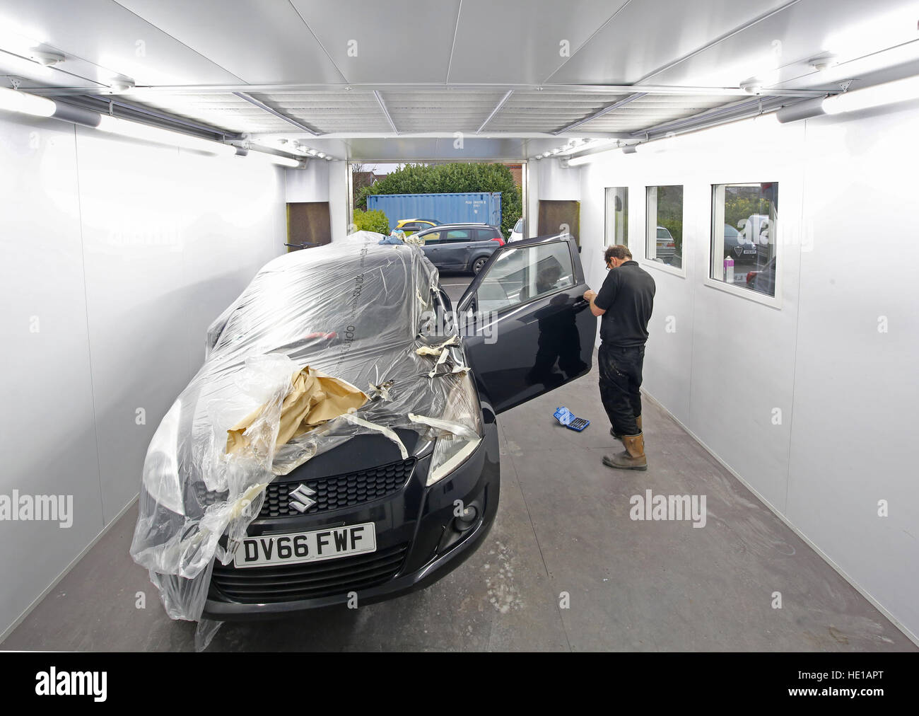 Un mécanicien dans un atelier de réparation de carrosserie après peinture masquage supprime les numéros de plaque (modifié) Banque D'Images