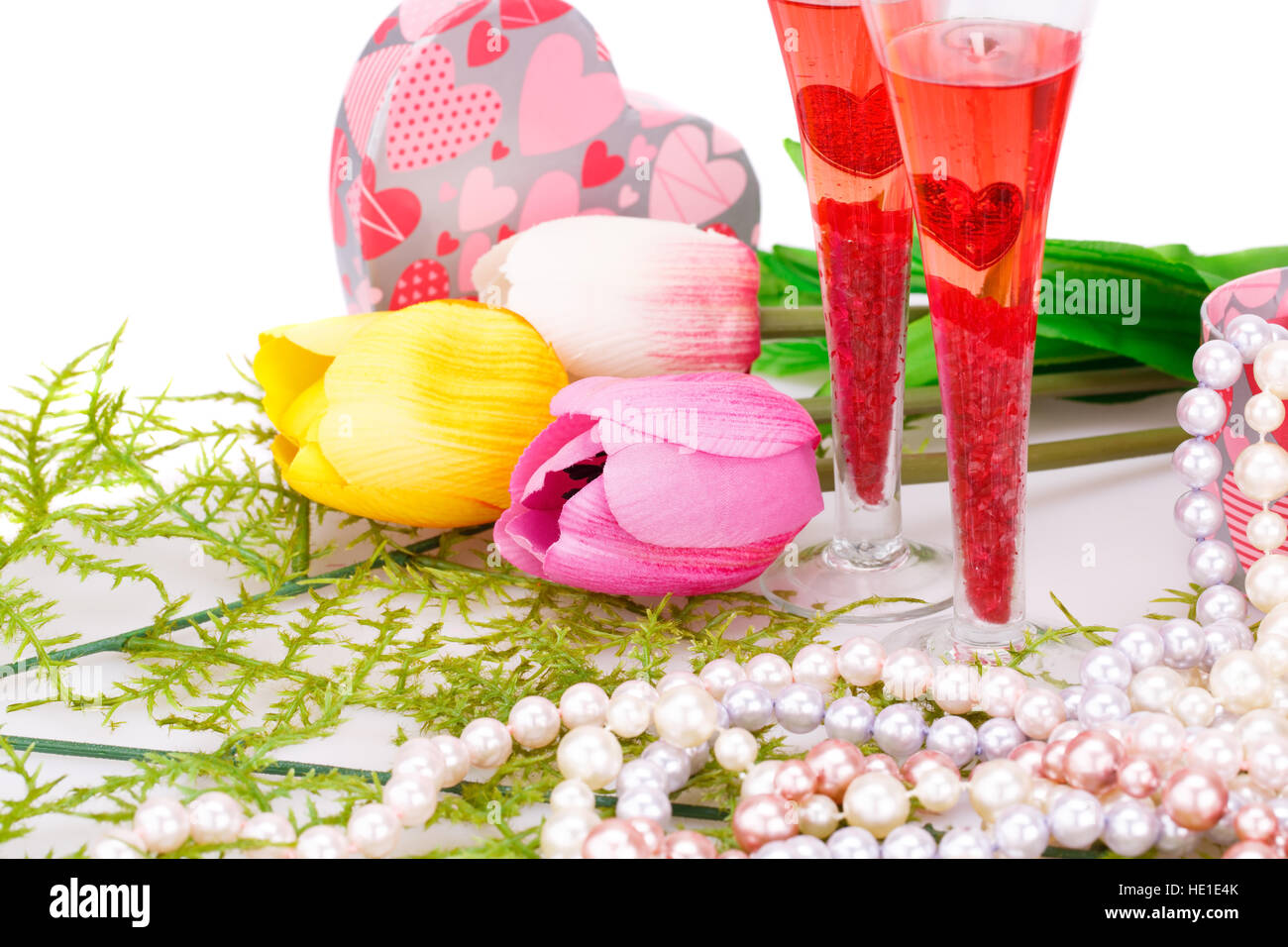 Deux verres, fleurs, colliers de perles colorées et boîte-cadeau sur fond blanc. Banque D'Images