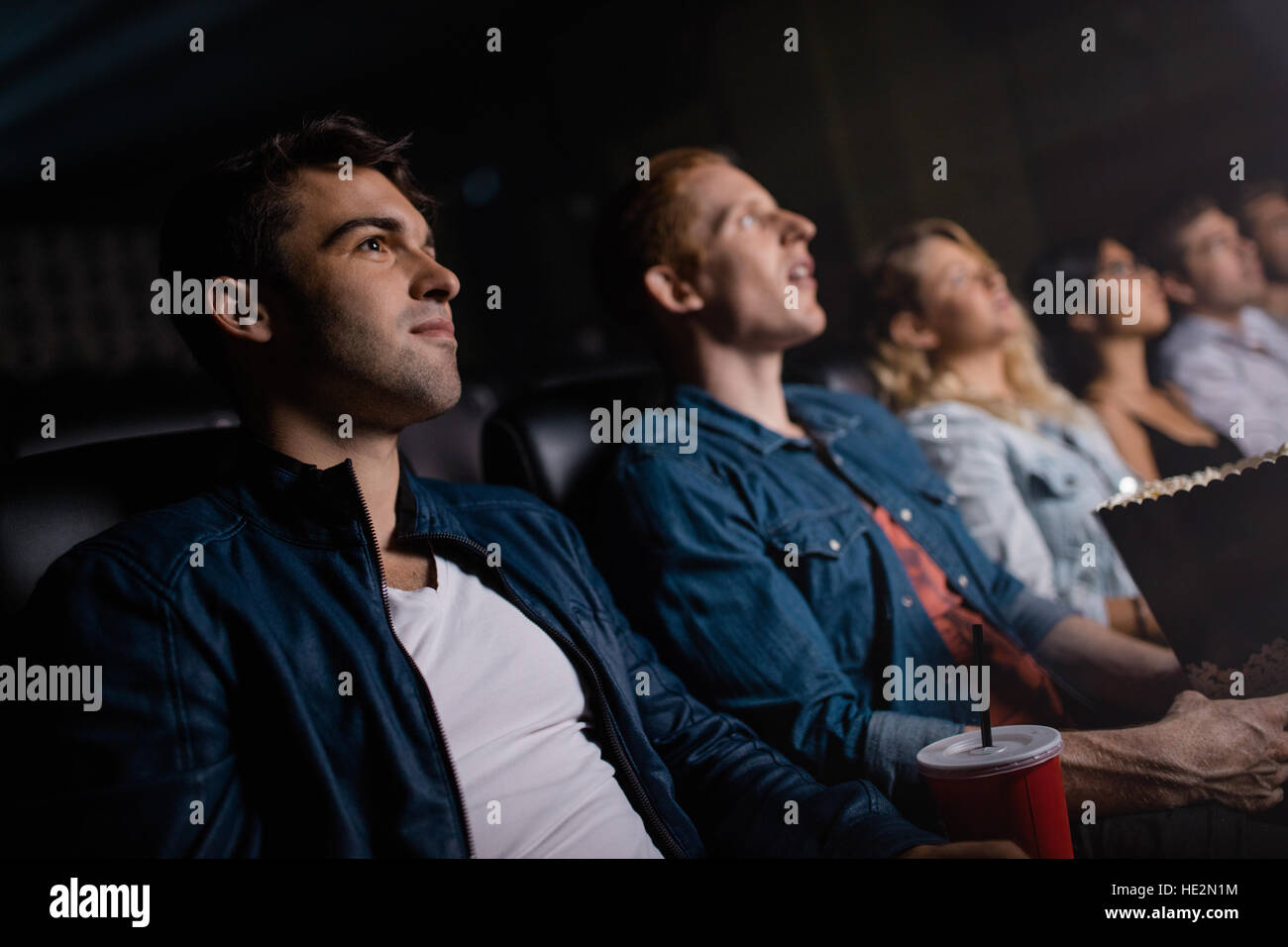 Jeune homme avec des amis regarder la vidéo dans le cinéma. Groupe de personnes au théâtre multiplexé. Banque D'Images