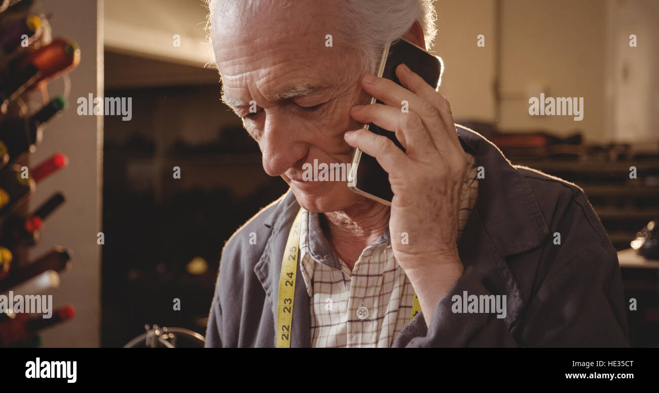 Shoemaker en conversation sur le téléphone mobile dans l'atelier Banque D'Images