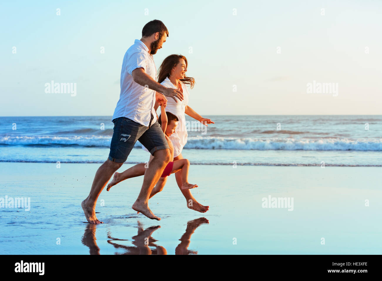 Happy Family - père, mère, fils de bébé tenir la main, exécutés en même temps par l'eau de mer le long de la piscine Sunset surf sur la plage de sable noir Banque D'Images
