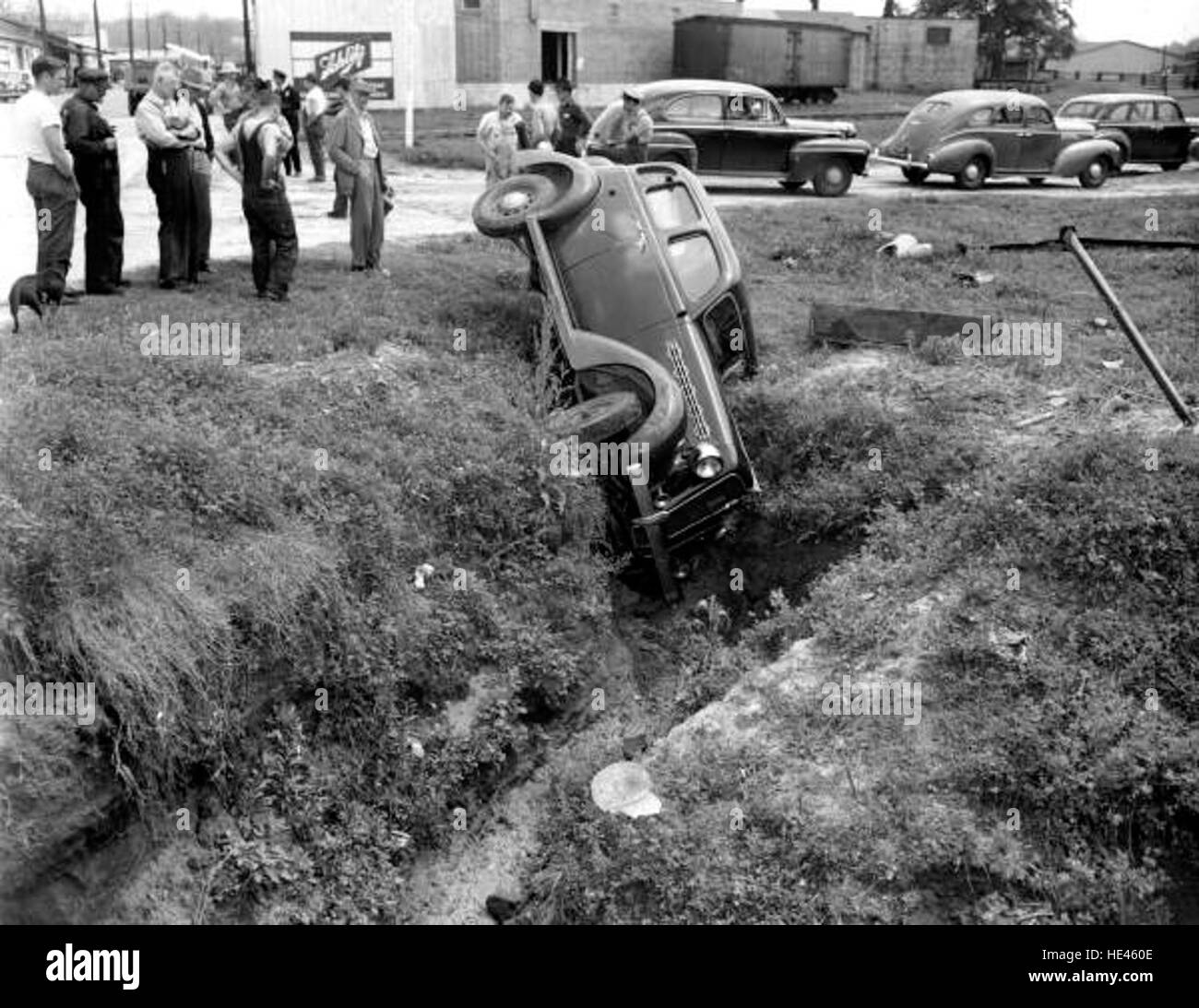 Cette photo historique capture une petite foule observant une voiture naufragée dans un fossé, un instantané d'une époque révolue mettant en valeur les conséquences d'un accident de la circulation. Banque D'Images