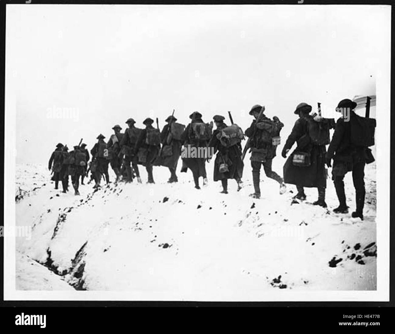 Cette photographie historique représente des soldats se dirigeant vers les tranchées en temps de guerre, se faufilant dans la neige profonde. L'image capture les conditions difficiles du champ de bataille pendant l'hiver. Banque D'Images