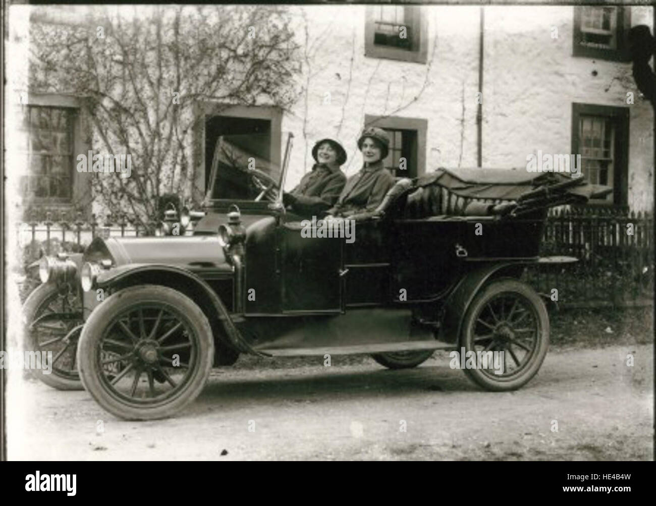 Cette photographie vintage montre deux femmes assises dans une voiture à moteur, capturant une ère révolue des débuts de l'histoire automobile. L'image reflète les normes sociales et la mode du passé, soulignant l'élégance et le charme de l'époque. Banque D'Images