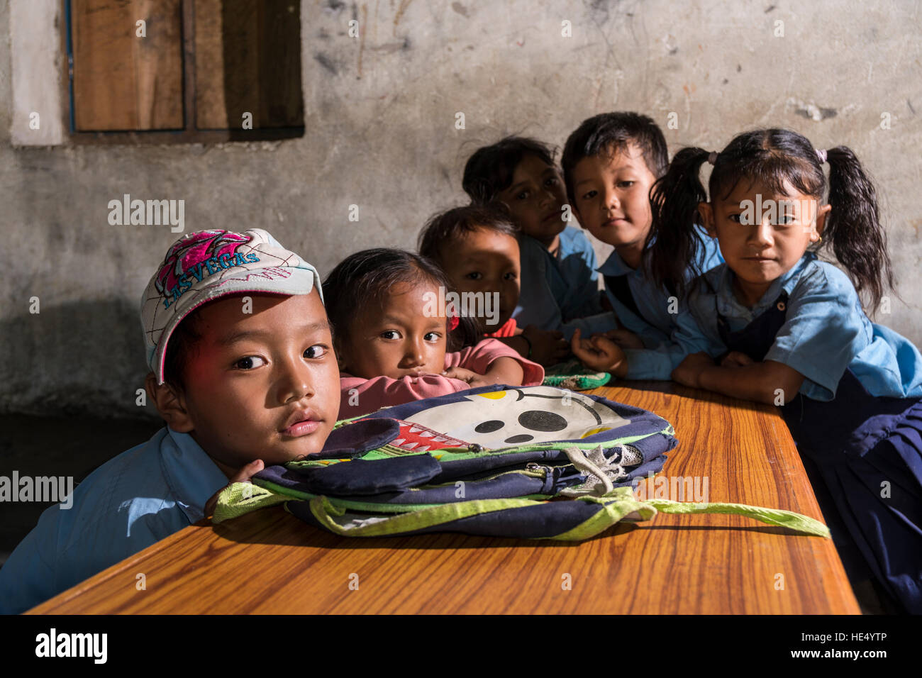Un groupe d'enfants en robe bleue, est assis à une table dans l'école locale Banque D'Images