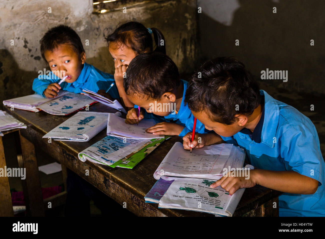 Un groupe d'enfants en robe bleue, est assis à une table dans l'école locale, étudiant Banque D'Images