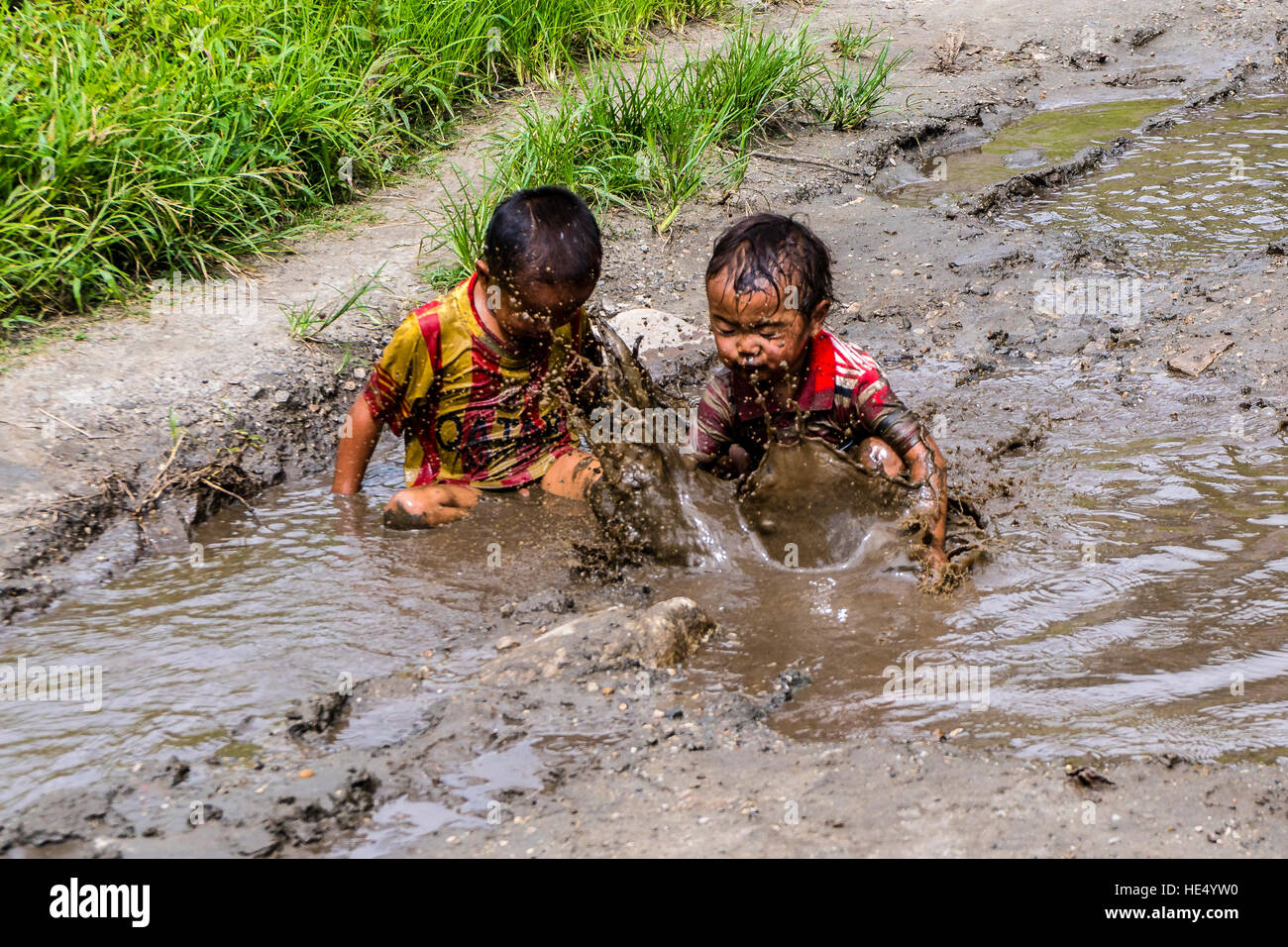 Les deux garçons, seuls port shirts, jouent dans la boue d'un étang Banque D'Images