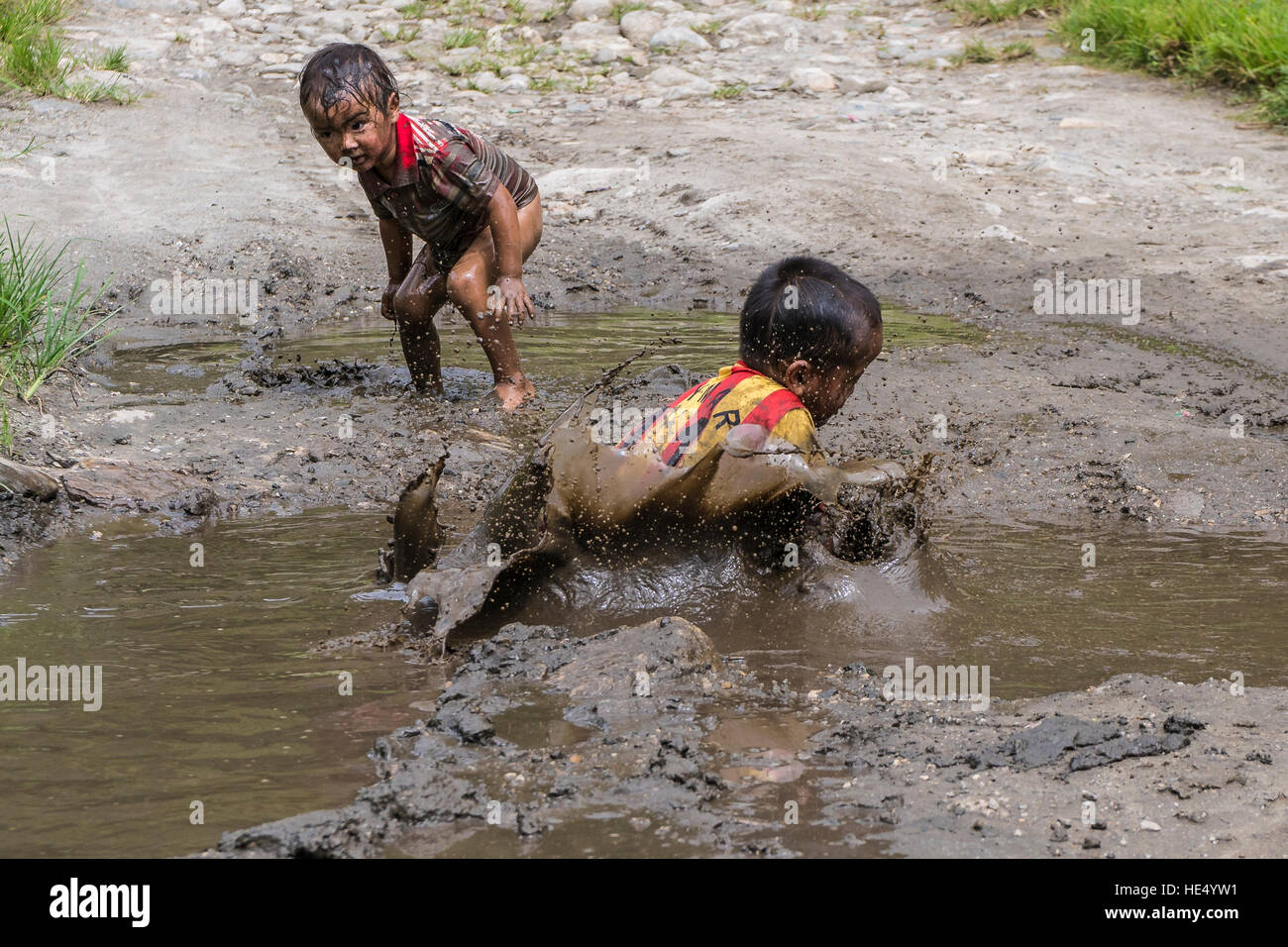 Les deux garçons, seuls port shirts, jouent dans la boue d'un étang Banque D'Images