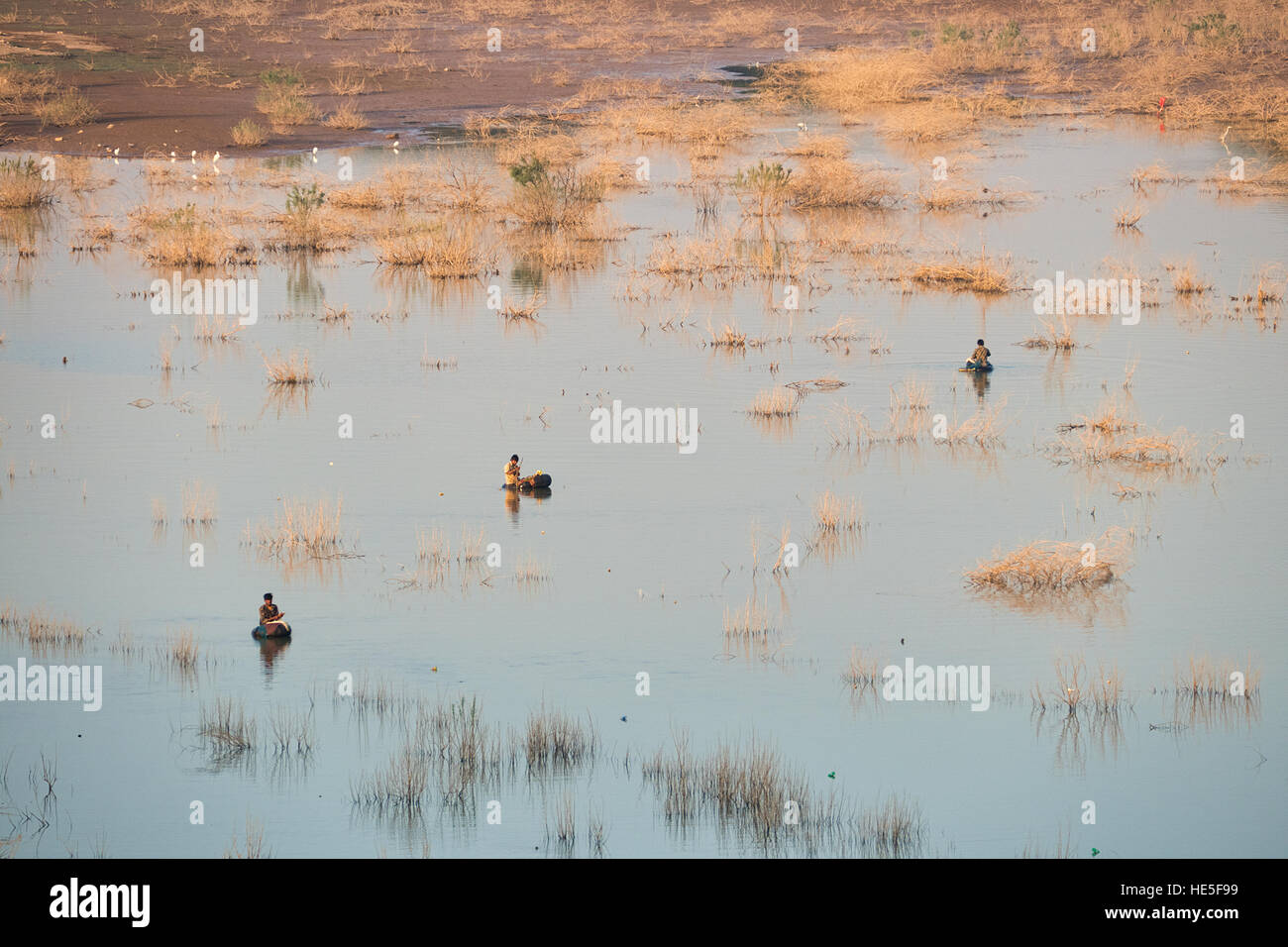 Trois pêcheurs pêche faire individuellement dans l'eau du bassin versant avec des arbustes secs et d'oiseaux blancs Banque D'Images