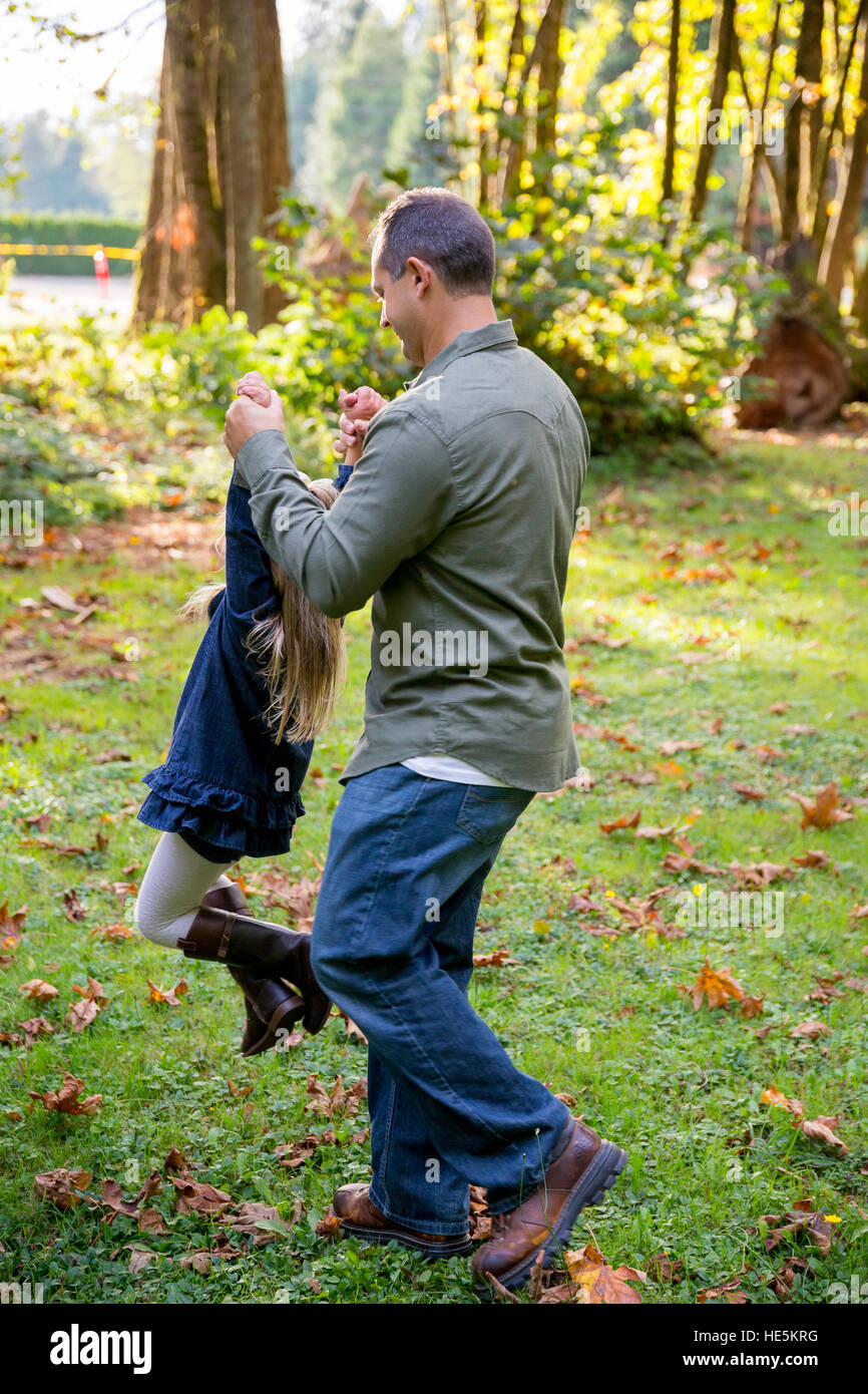 Papa se balançant autour de sa jeune fille par les bras tandis que le jeu et le plaisir à un parc naturel. Banque D'Images