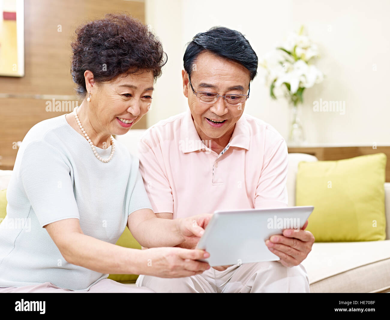Senior asian couple sitting on couch looking at tablet computer ensemble, heureux et souriant Banque D'Images
