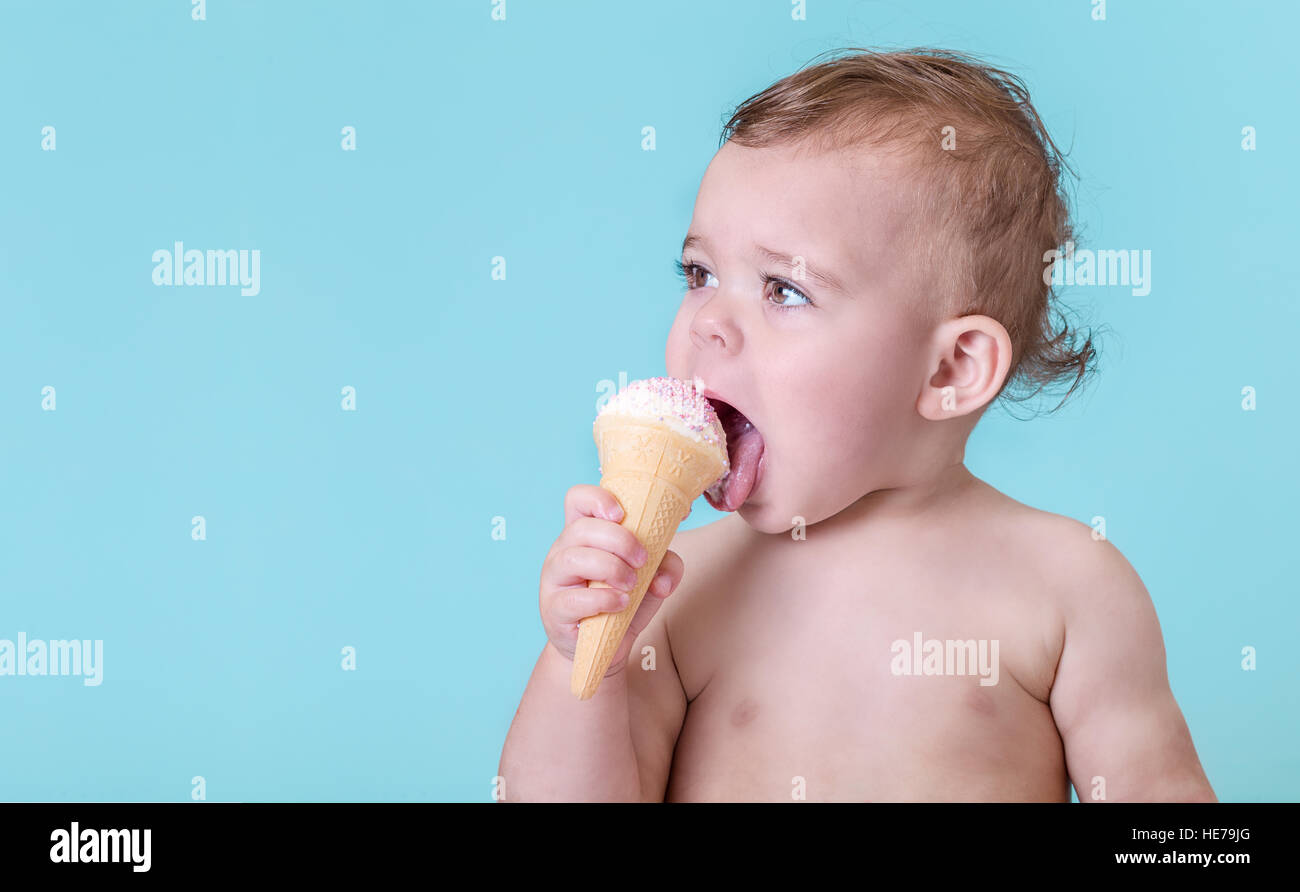 Adorable bébé fille manger une glace sur fond bleu clair Banque D'Images