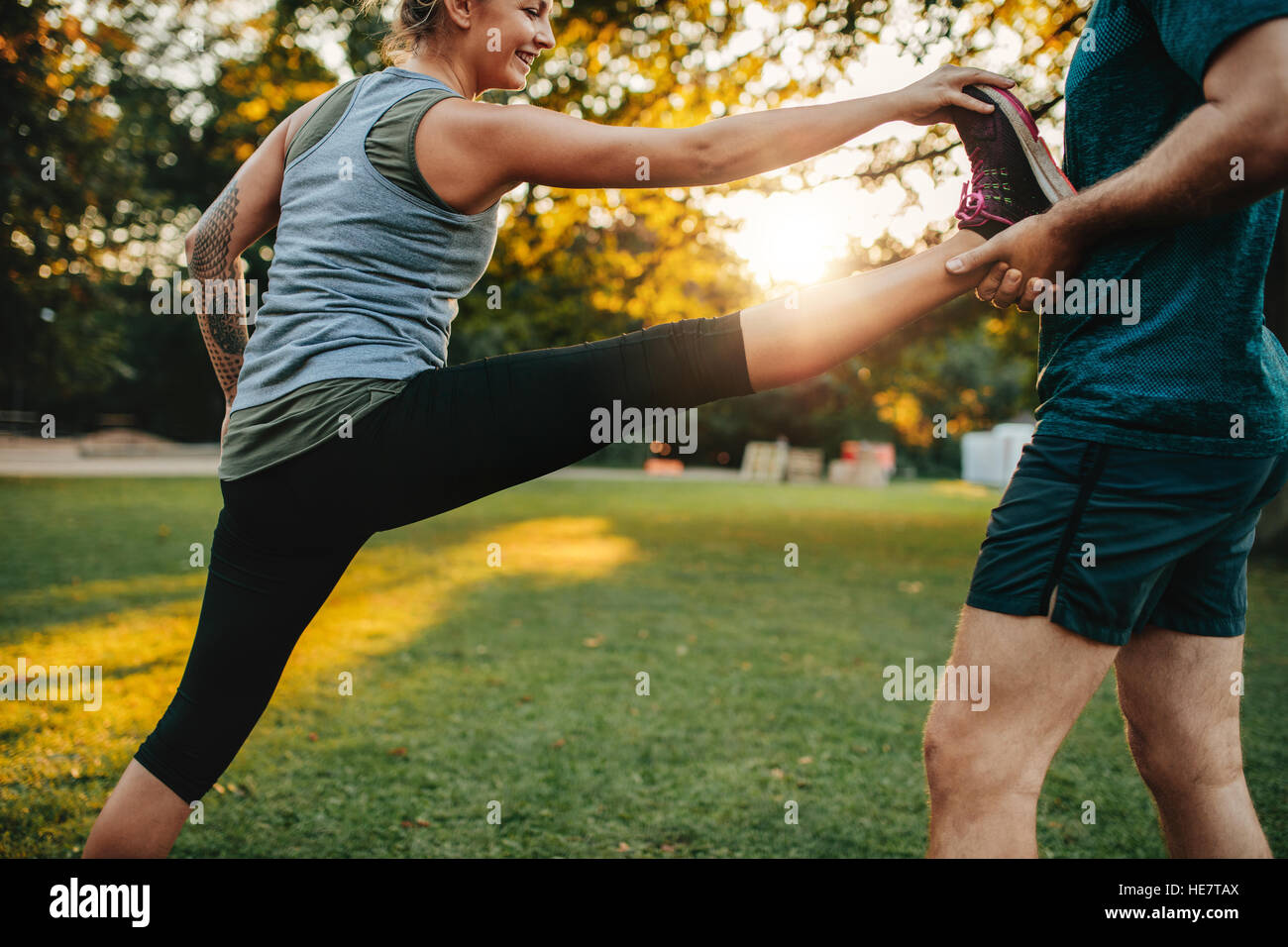 Fit young woman doing stretching exercices avec l'aide d'un entraîneur personnel en parc. Coach de jambe holding femelle. Banque D'Images