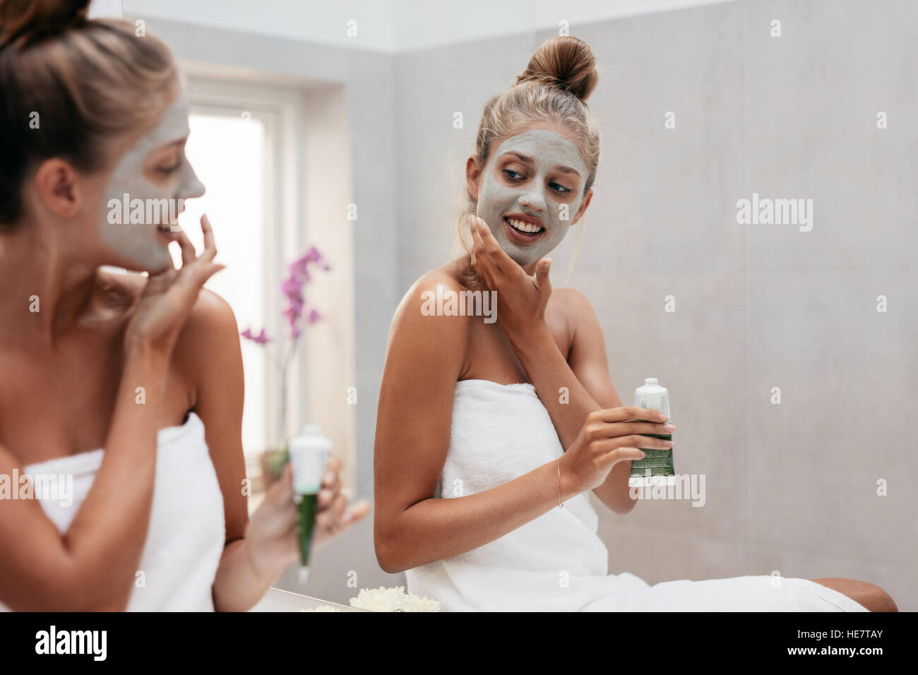 Happy young woman applying facepack dans la salle de bains. Femme à la recherche de miroir et de faire un soin de beauté. Banque D'Images