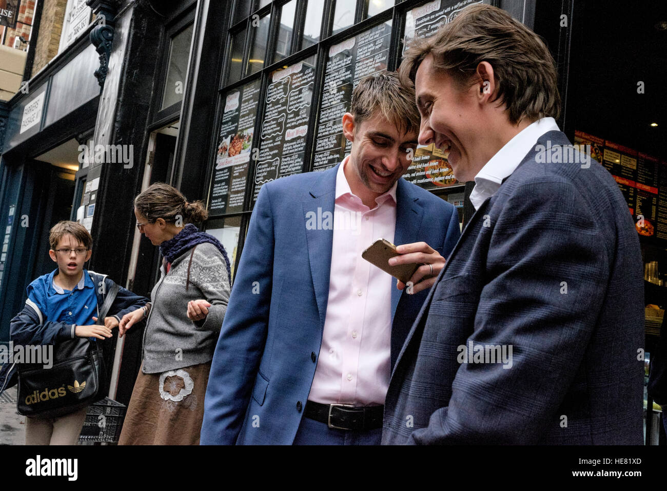 Deux hommes d'affaires à l'extérieur d'un pub de Londres partager un moment cocasse de leur téléphone mobile Banque D'Images