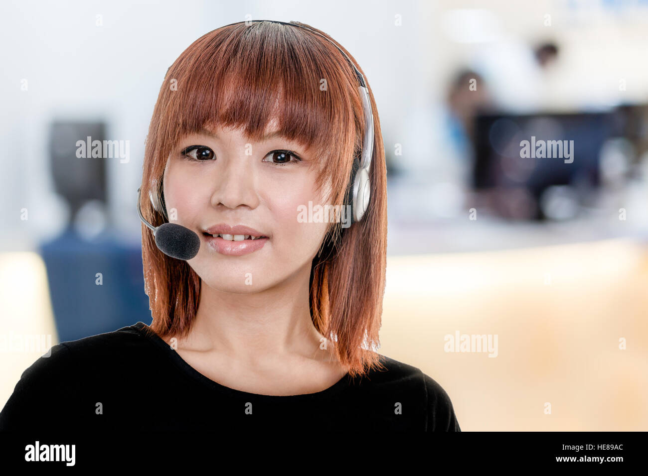 Femme d'origine asiatique portant un casque avec microphone avec bureau centre d'appel ou de flou artistique en arrière-plan Banque D'Images