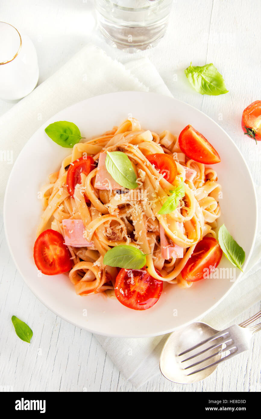 Tagliatelle avec du jambon, sauce tomate, tomates cerise et les feuilles de basilic sur plaque blanche - délicieux plats de pâtes faites maison Banque D'Images