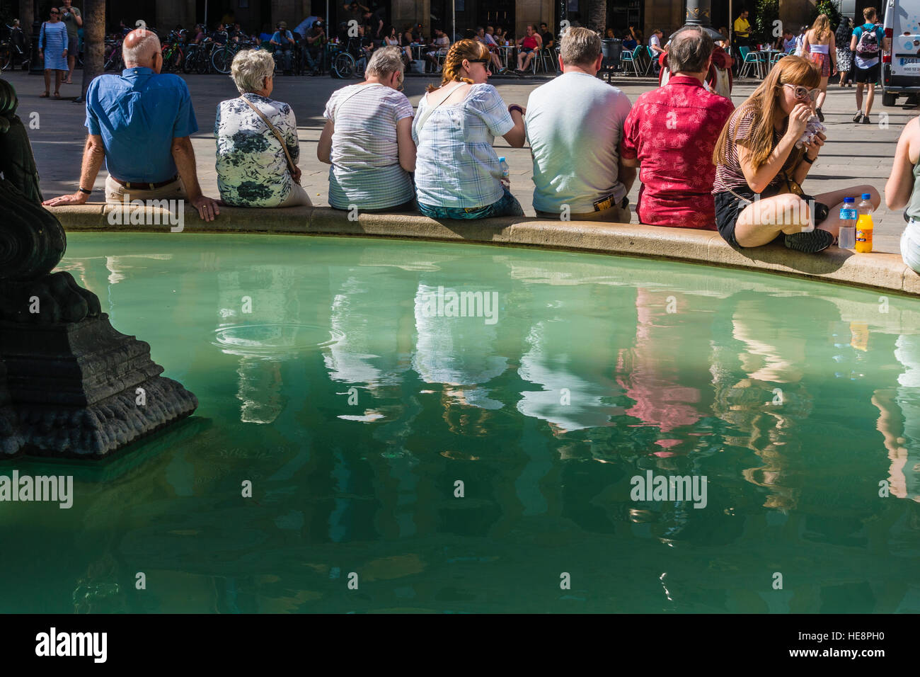Une rangée de touristes fatigués sont assis côte à côte sur le bord d'une fontaine, sous l'eau, pour se détendre dans un plaza à Barcelone, Espagne. Banque D'Images