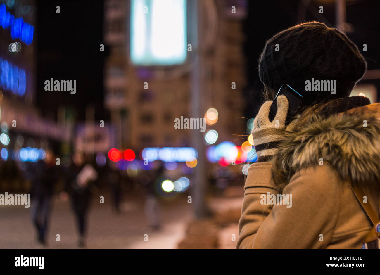 Fille en chapeau et des gants talking on mobile phone de nuit contre les lumières de la ville floues en hiver Banque D'Images