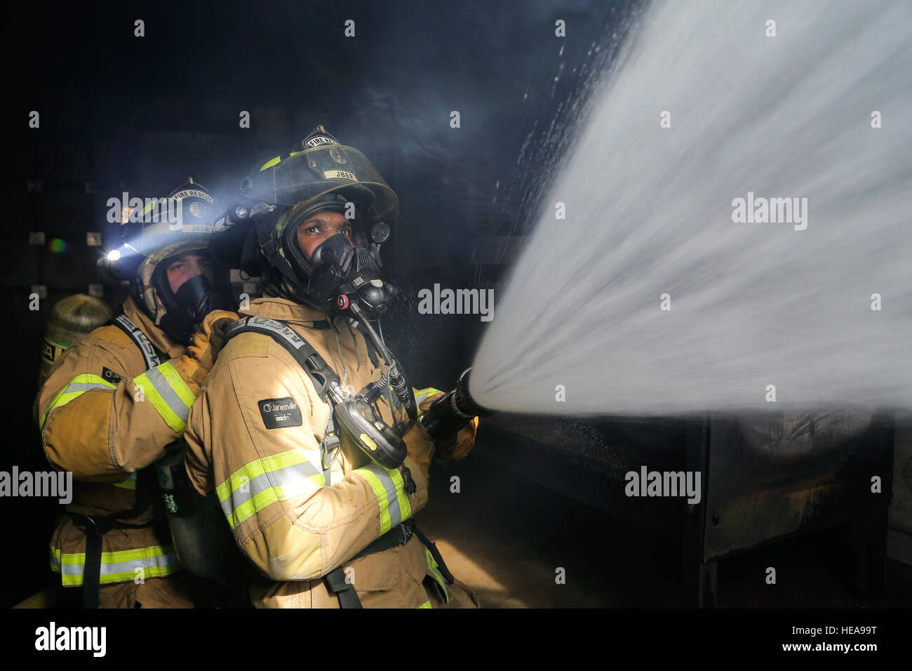 Les cadres supérieurs de l'US Air Force Airman Danny Russo, à gauche, et d'un membre de la 1re classe Larry Kyles, protection contre l'incendie spécialistes chargés de la 673e Escadron de génie civil, utiliser un tuyau d'eau pour ventiler une pièce emplie de fumée, alors que la formation dans le simulateur de tir réel à Joint Base Elmendorf-Richardson, Alaska, le 13 avril 2016. Le service d'incendie de JBER est formé pour répondre à diverses urgences et effectue régulièrement des exercices de maintien en puissance de maintenir les compétences et l'état de préparation opérationnelle. Alejandro Pena) Banque D'Images