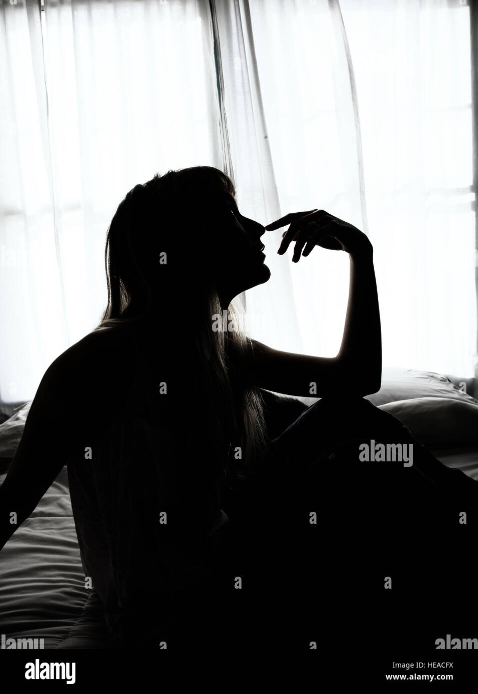 Silhouette of woman sitting in bed by window Banque D'Images