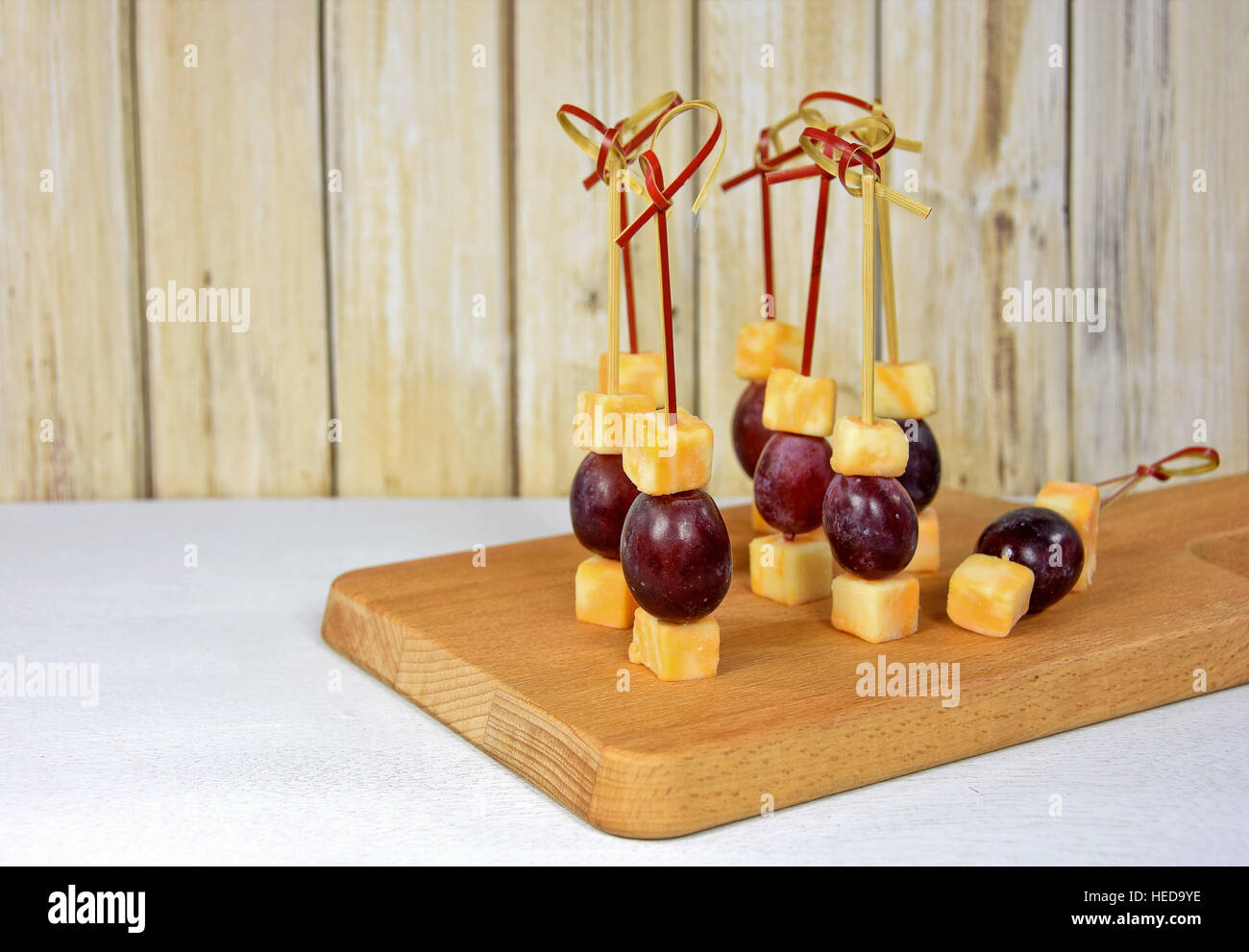 Les raisins rouges et fromage apéritif sur bambou stick sur une planche à découper en bois Banque D'Images