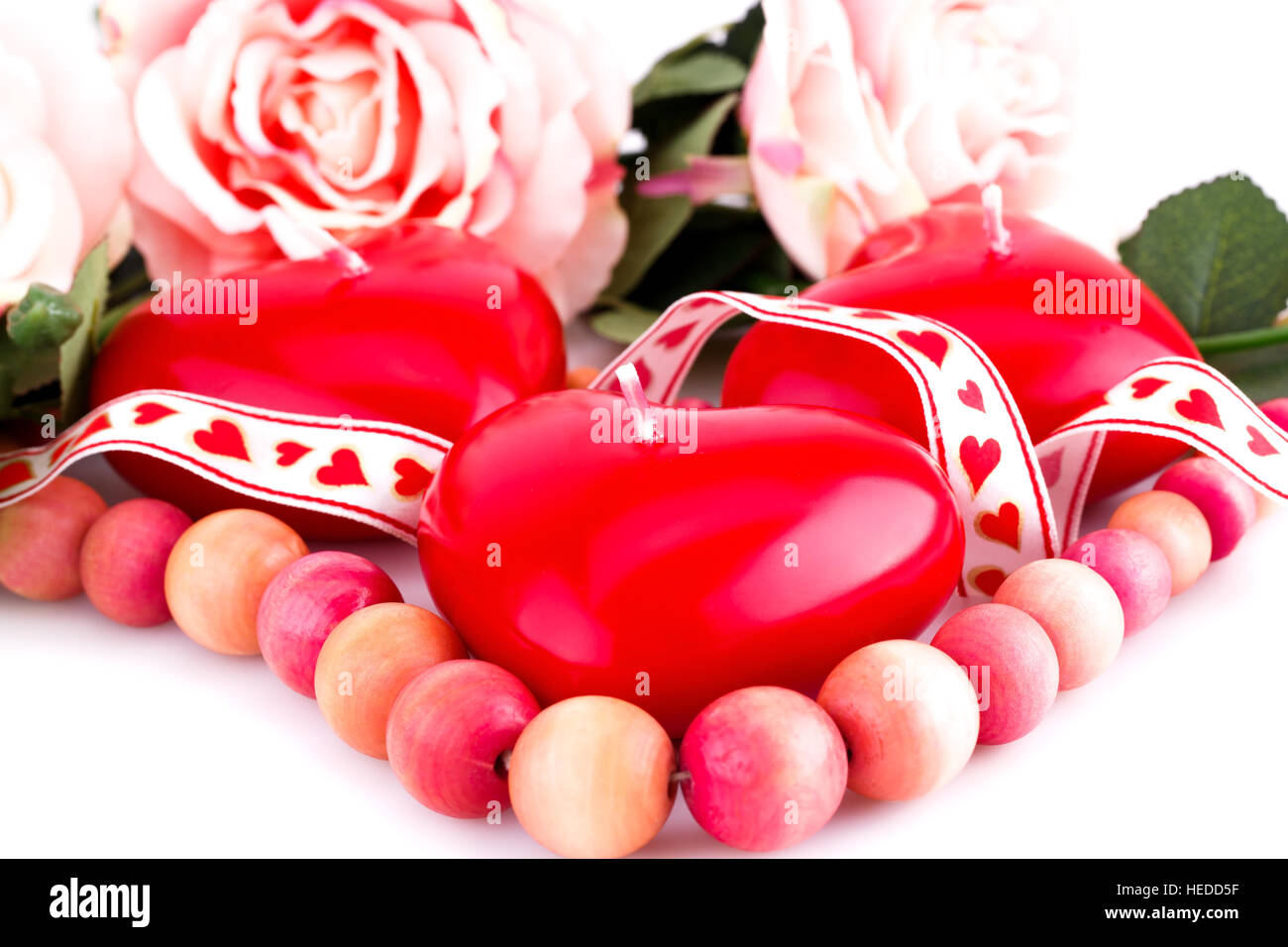 Coeur rouge en bois, bougies, collier ruban et roses sur fond blanc. Banque D'Images