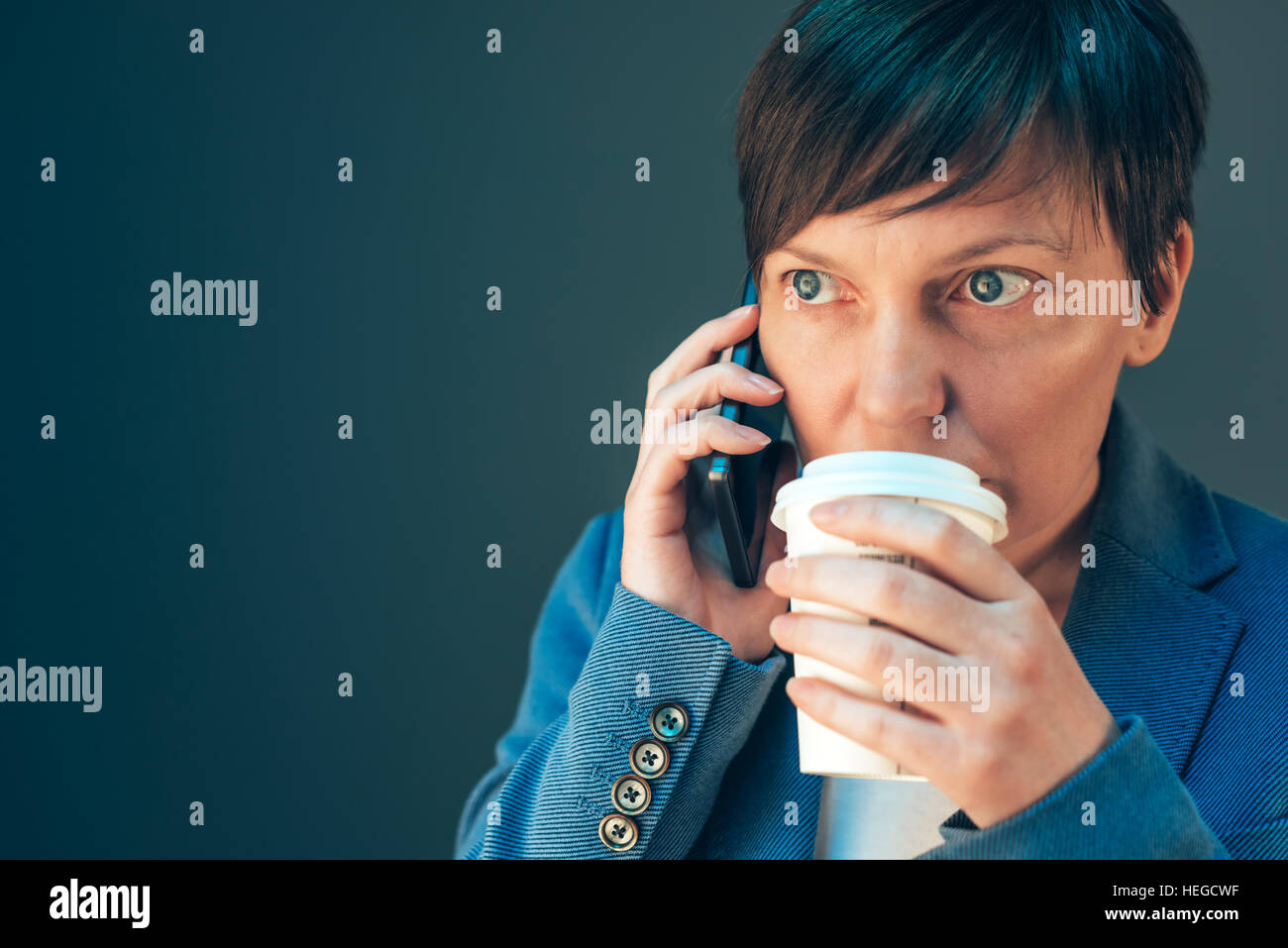 Young adult businesswoman drinking coffee pour aller et talking on mobile phone Banque D'Images