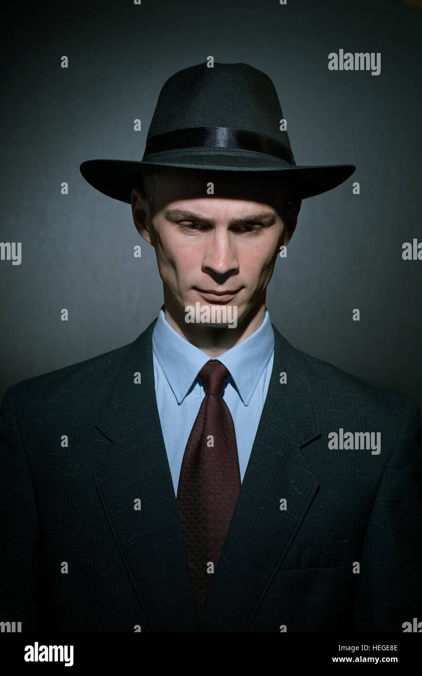 Beau jeune homme à la mode détective dans un élégant costume et chapeau à la descendre avec un air sérieux sur un fond dégradé de gris Banque D'Images