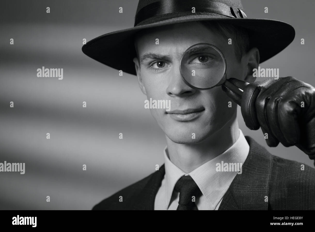 Portrait de gris d'un beau grave jeune détective intelligent dans un élégant style vintage hat holding une loupe à l'œil qu'il fixe Banque D'Images