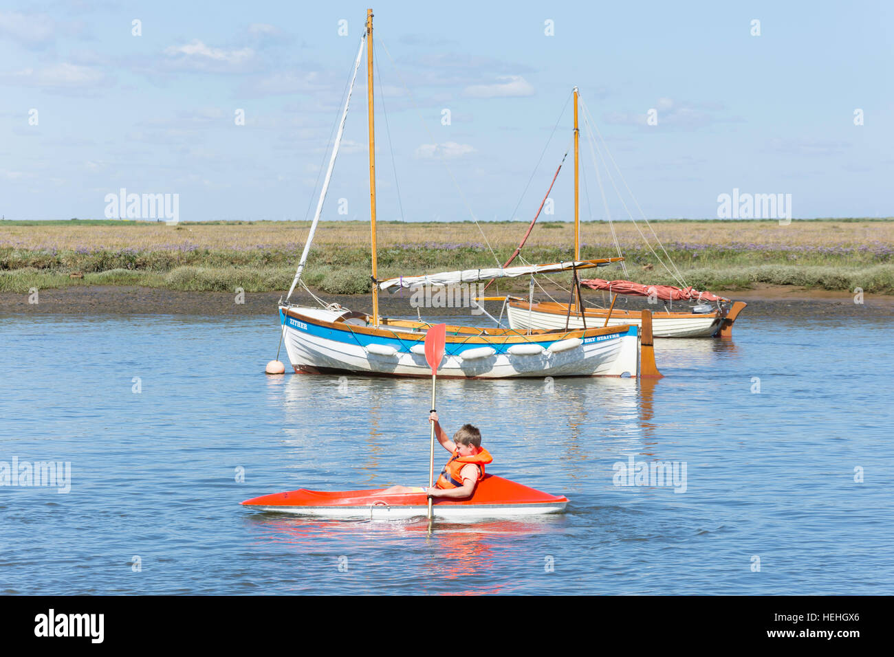 Jeune garçon en bateau à aubes sur la rivière brûler du quai, Burnham Overy Staithe, Norfolk, Angleterre, Royaume-Uni Banque D'Images