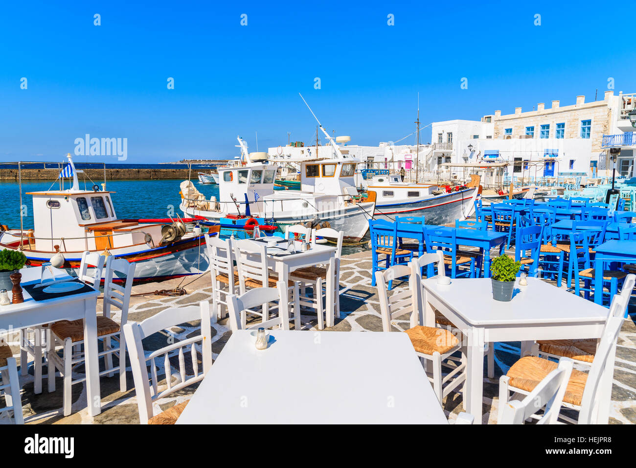 Tables de restaurant et des bateaux de pêche d'un ancrage dans le port de Naoussa, l'île de Paros, Grèce Banque D'Images