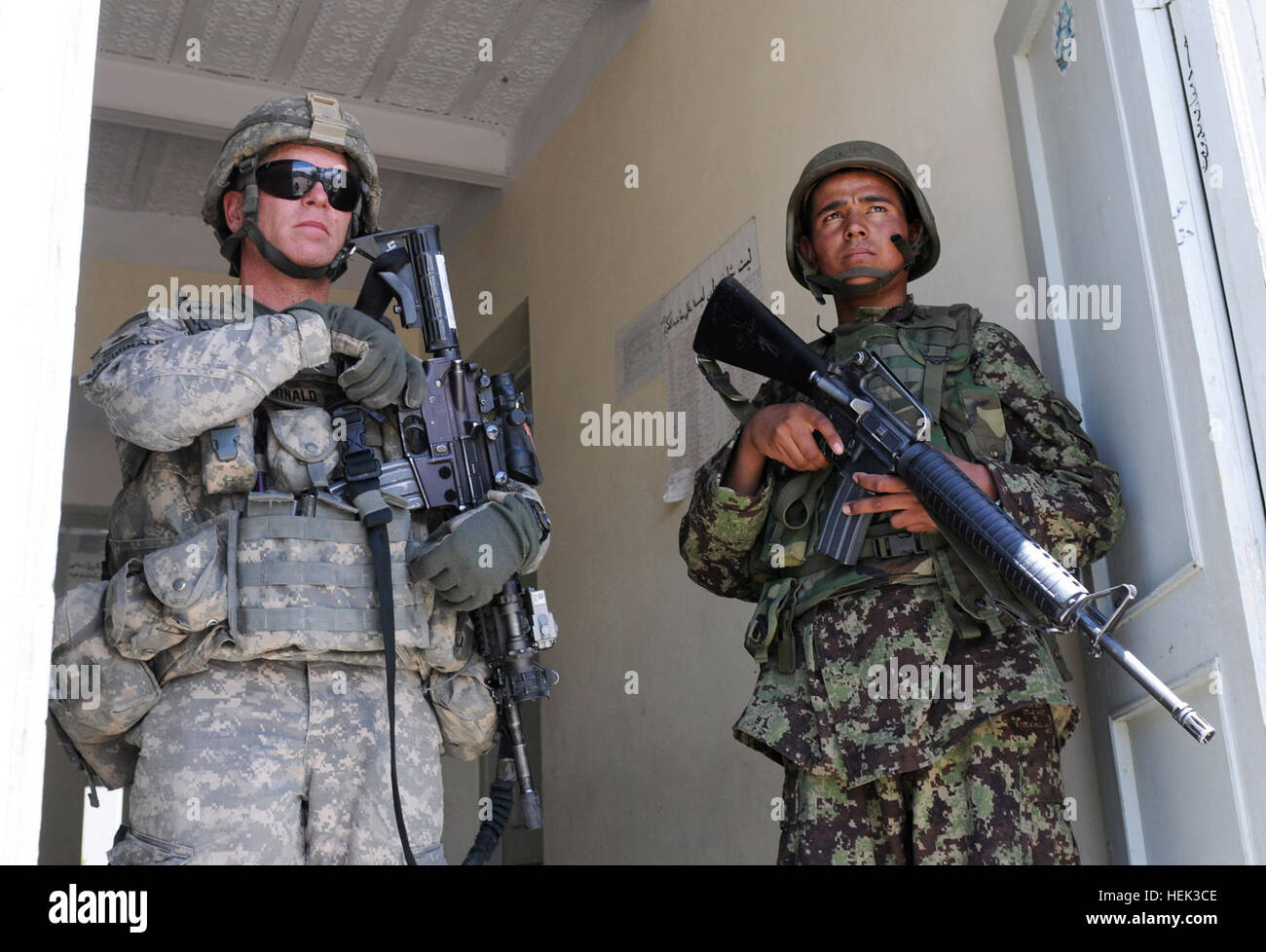 La province de Laghman - Un soldat de l'Armée nationale afghane avec 4e compagnie a, 1er Kandak, 1ère Brigade, 201e Corps, assure la sécurité du personnel de l'armée américaine avec le Sgt. Michael J. MacDonald de Canterbury, Conn., un chef d'équipe avec 2e peloton, Compagnie B, 1er Bataillon, 102e Régiment d'infanterie, Task Force gris fer, au cours d'une visite à Meya Abdul Karim l'école dans l'Est de l'Afghanistan, la province de Laghman 18 mai. Les responsables de l'école ont discuté de la sécurité, les préoccupations locales et leur interaction avec le gouvernement afghan au cours de la visite avec ANA et Internationale d'assistance à la sécurité. Le campus, qui abrite une jeune fille schoo Banque D'Images