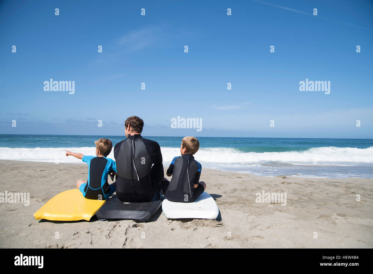 Vue arrière de l'homme et ses deux fils assis sur bodyboards pointant, Laguna Beach, Californie, USA Banque D'Images