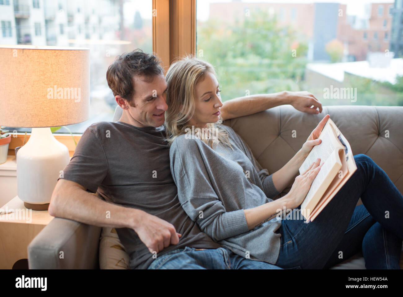 Couple reclining on sofa reading a book Banque D'Images