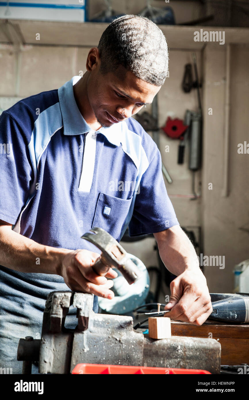 Jeune homme hammering nail en atelier de réparation Banque D'Images