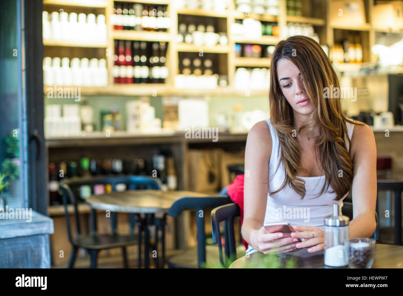 Young woman sitting in cafe lecture textes smartphone Banque D'Images