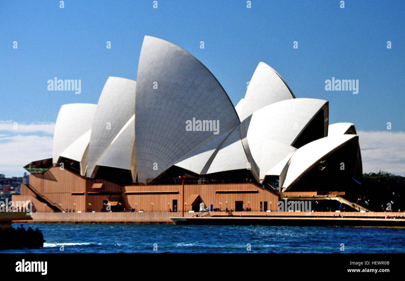Une image vibrante capturant l'Opéra de Sydney et ses voiles blanches emblématiques, ainsi que des reflets de son architecture moderniste dans l'eau environnante. Cette photographie met en valeur les monuments culturels de Sydney. Banque D'Images